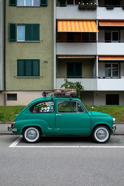 During the day, green Volkswagen beetle is parked on the green and white concrete building
